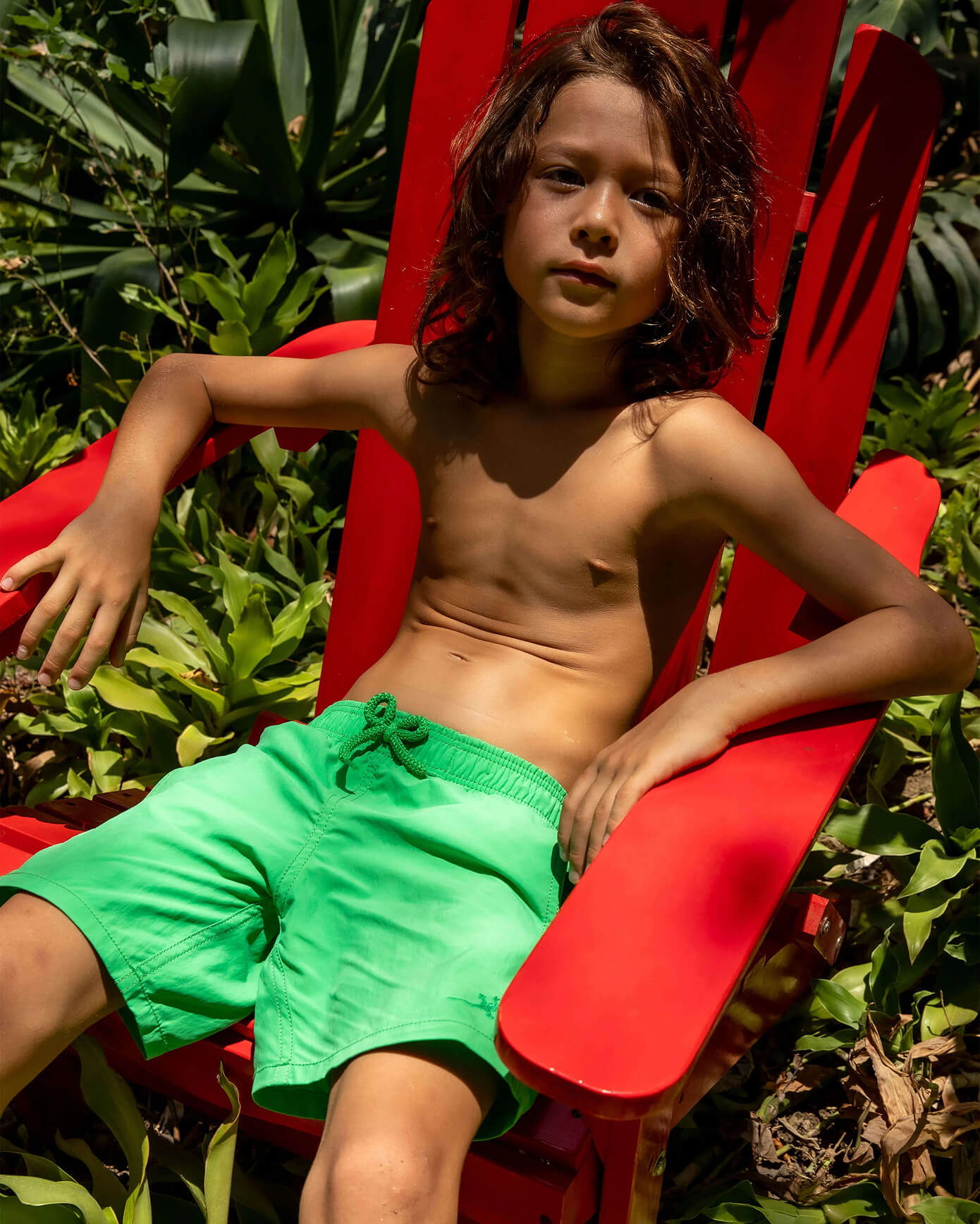 Relajación en silla roja Niño descansando en silla roja con bañador verde.